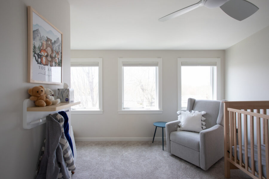 Twin Cities home renovation reveals a bright nursery. It includes a crib, glider, wall shelf, and natural light.
