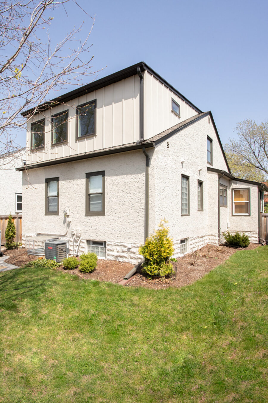 Renovated home exterior features white stucco, beige vertical panel siding, dark trim accents.