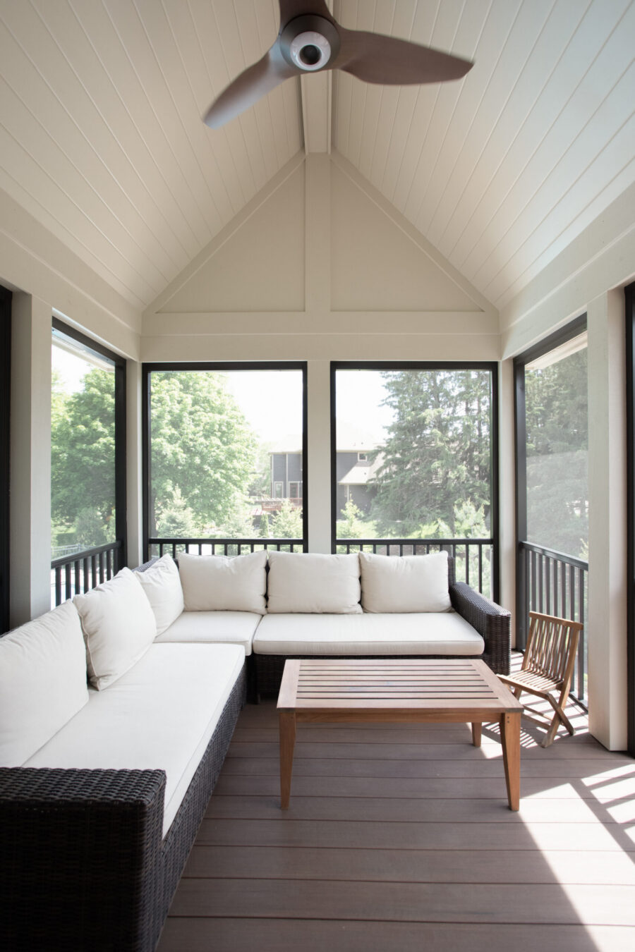 Vaulted screened porch, part of a home renovation, features a ceiling fan, composite decking, and a woven sectional sofa.