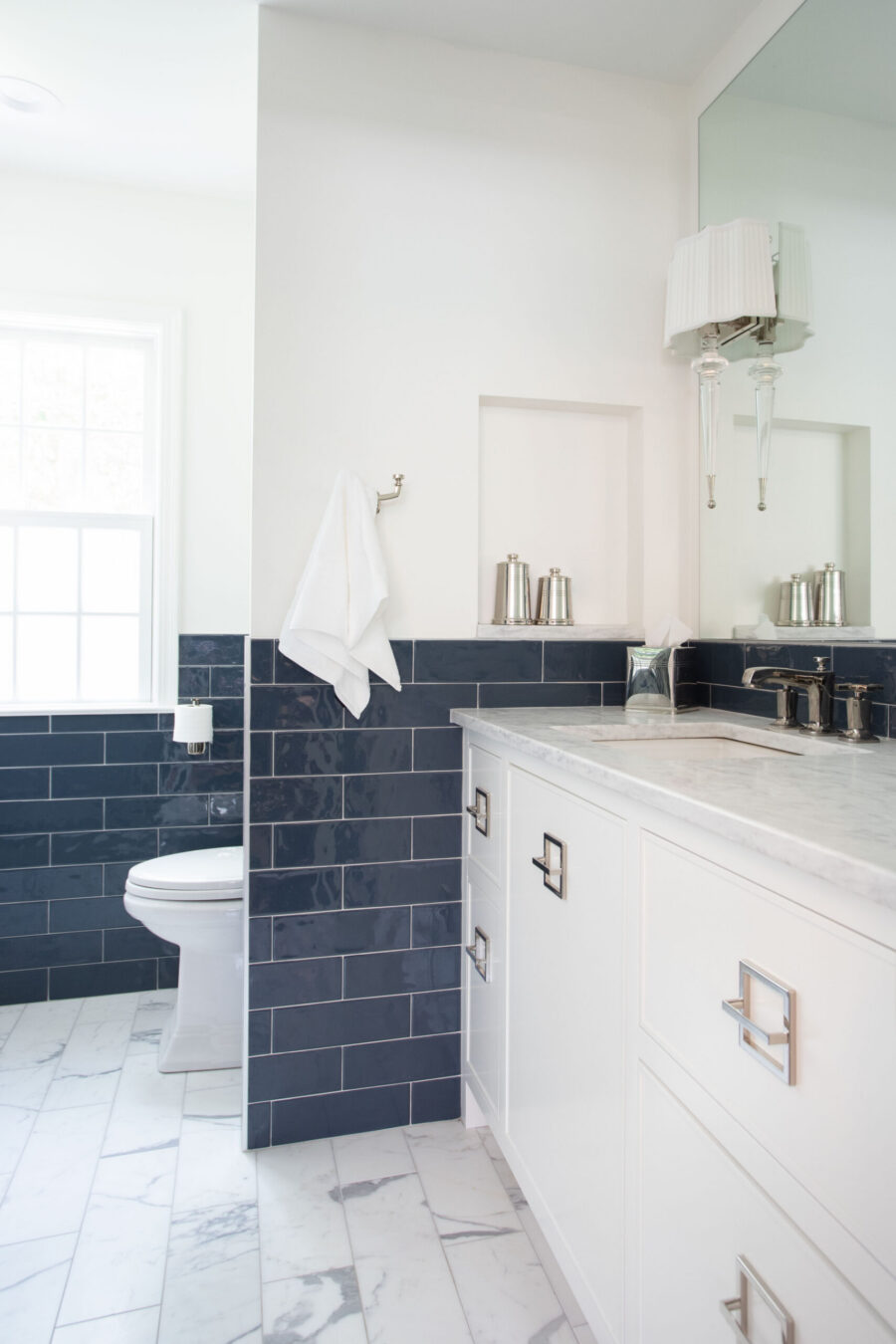 Twin Cities bathroom remodel features navy subway tile, white marble floor, and a white vanity. Window light illuminates the space.