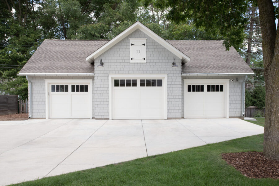 Gray shingle three-car garage features bright white doors, gooseneck lights.