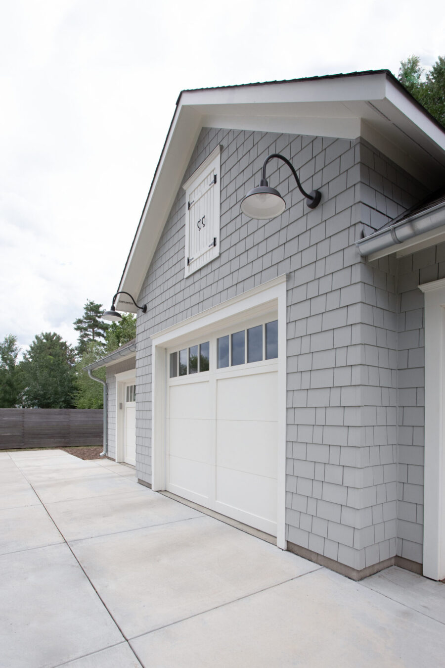 New gray shingle garage features white trim and doors. Black gooseneck lighting brightens the renovated exterior.