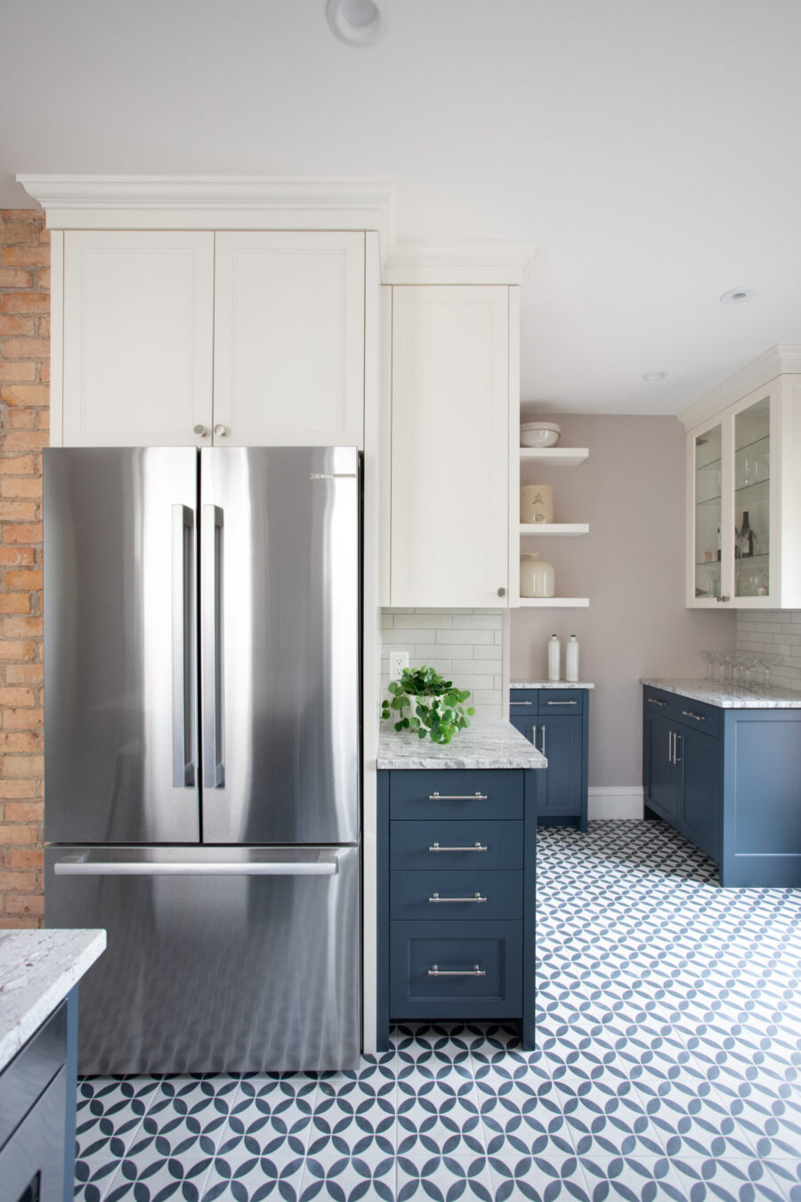 Vibrant kitchen renovation pairs white, blue cabinetry, steel fridge, geometric floor design.