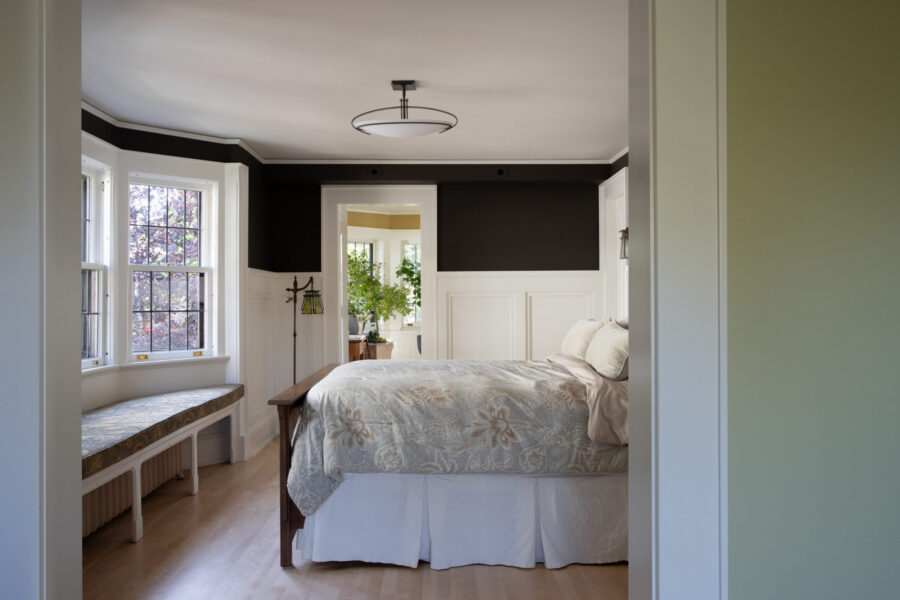 This bright Twin Cities bedroom remodel features dark upper walls, white wainscoting, wood floors, and a bay window seat.