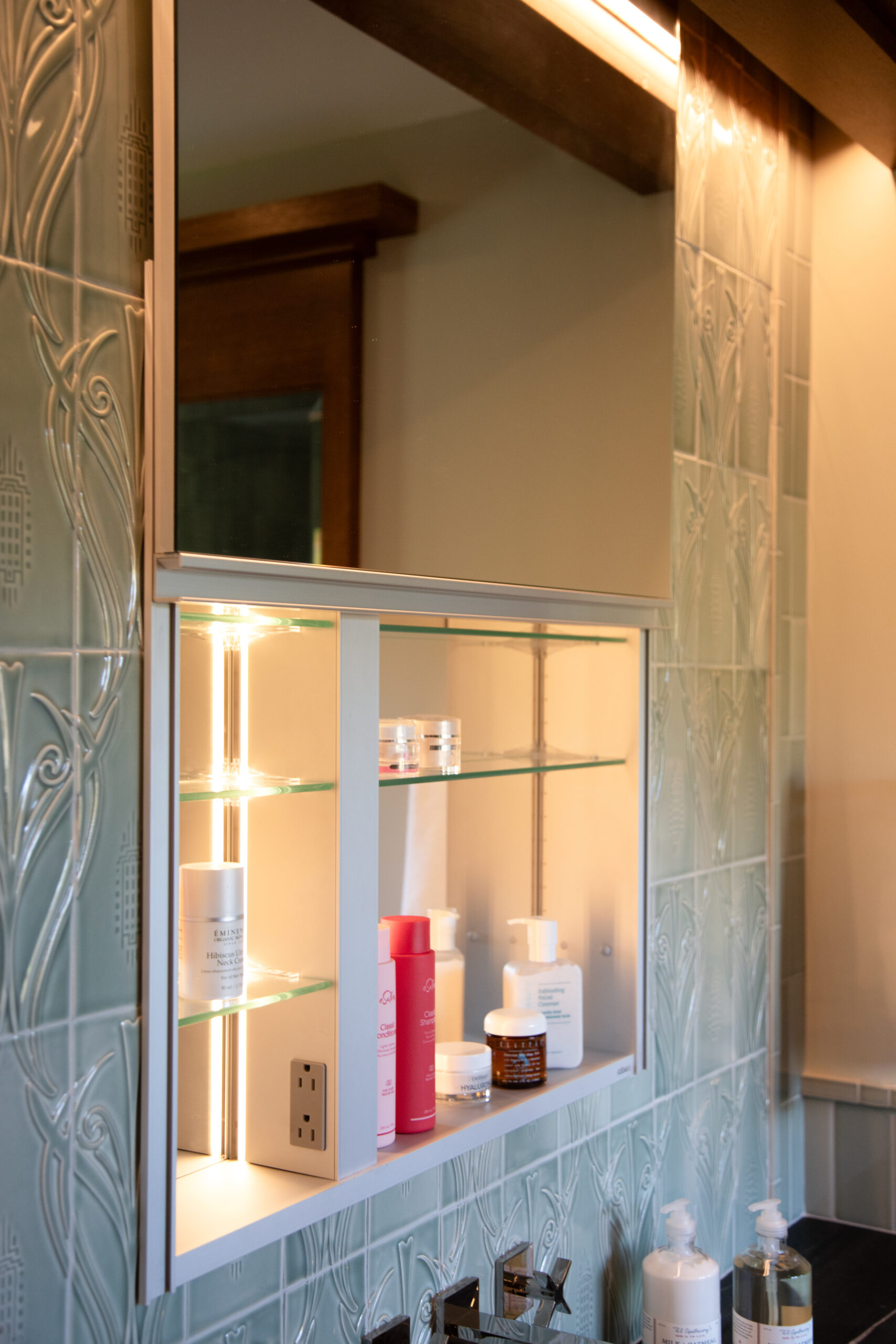 Warm-lit glass-shelf medicine-cabinet has embossed tile, toiletries, bathroom-remodel.