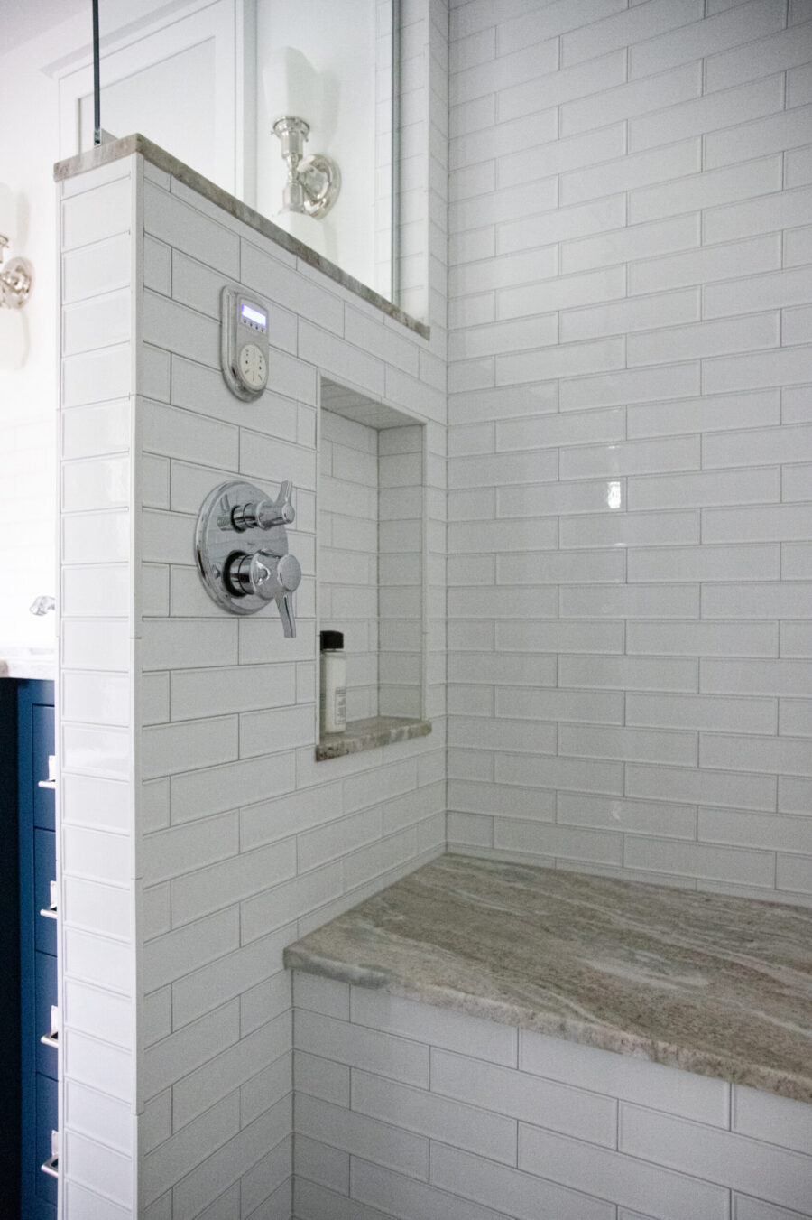 Contemporary bright white subway-tiled bathroom shower contains built-in granite seating.