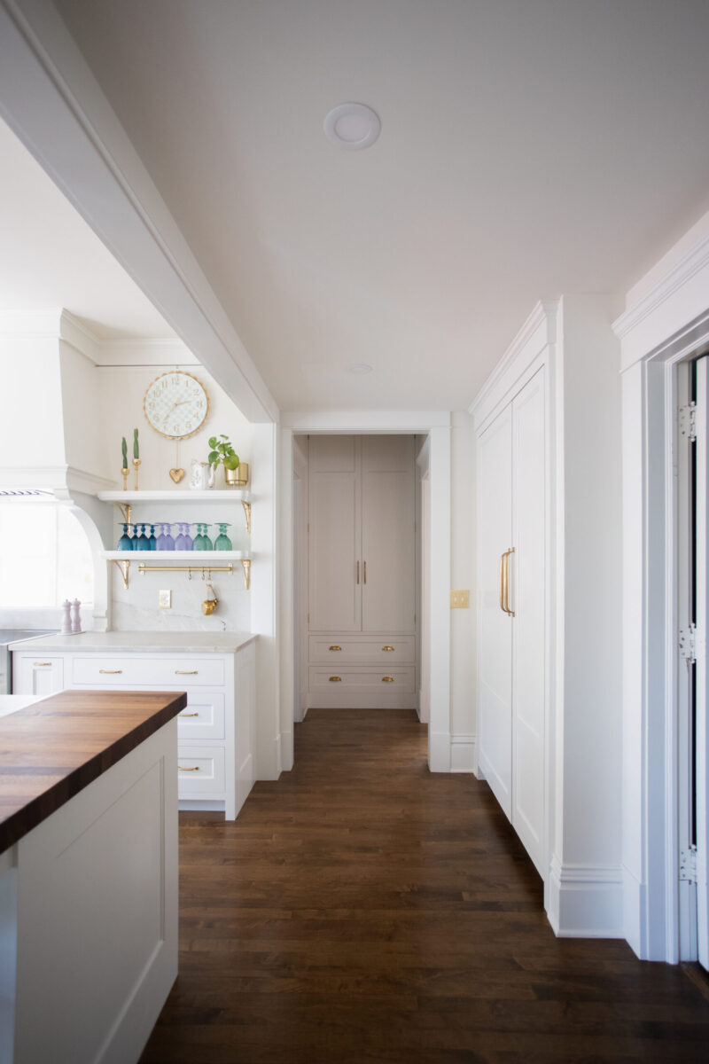Bright kitchen remodel connects to a long hallway, featuring white built-in cabinetry, dark wood floors, and brass accents in Twin Cities.
