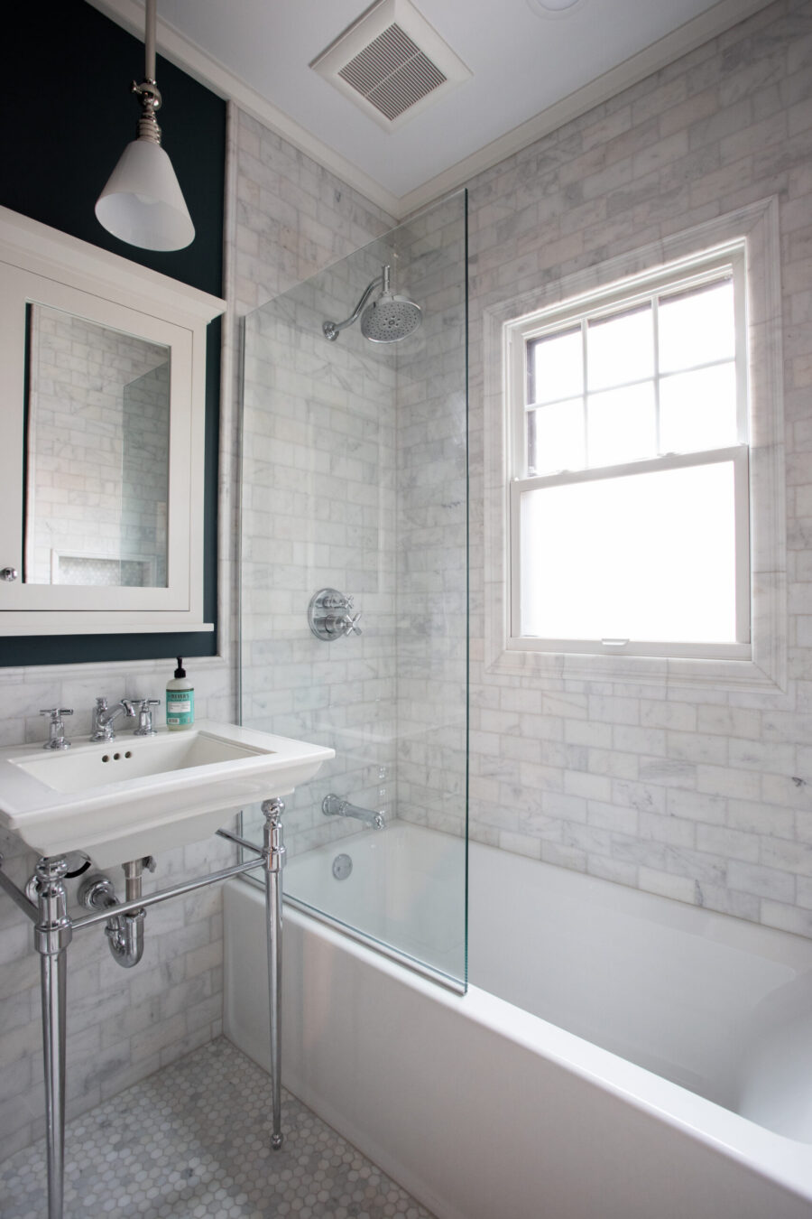 Contemporary bathroom remodel highlights white marble, glass shower, chrome pedestal sink.