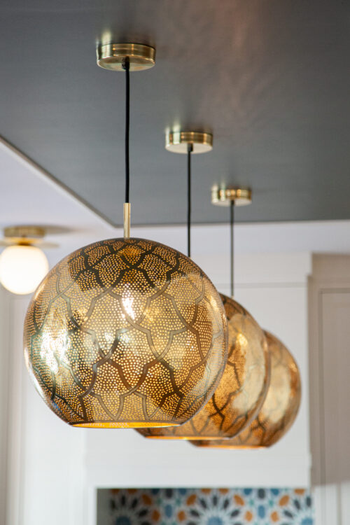 Intricately-perforated-brass-globe-pendants hang from dark-painted ceiling over tiled kitchen-remodel island