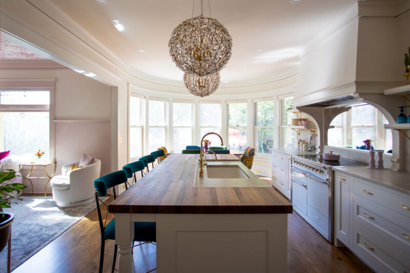Twin Cities kitchen remodel displays a long wood island, crystal chandeliers, and bay windows.