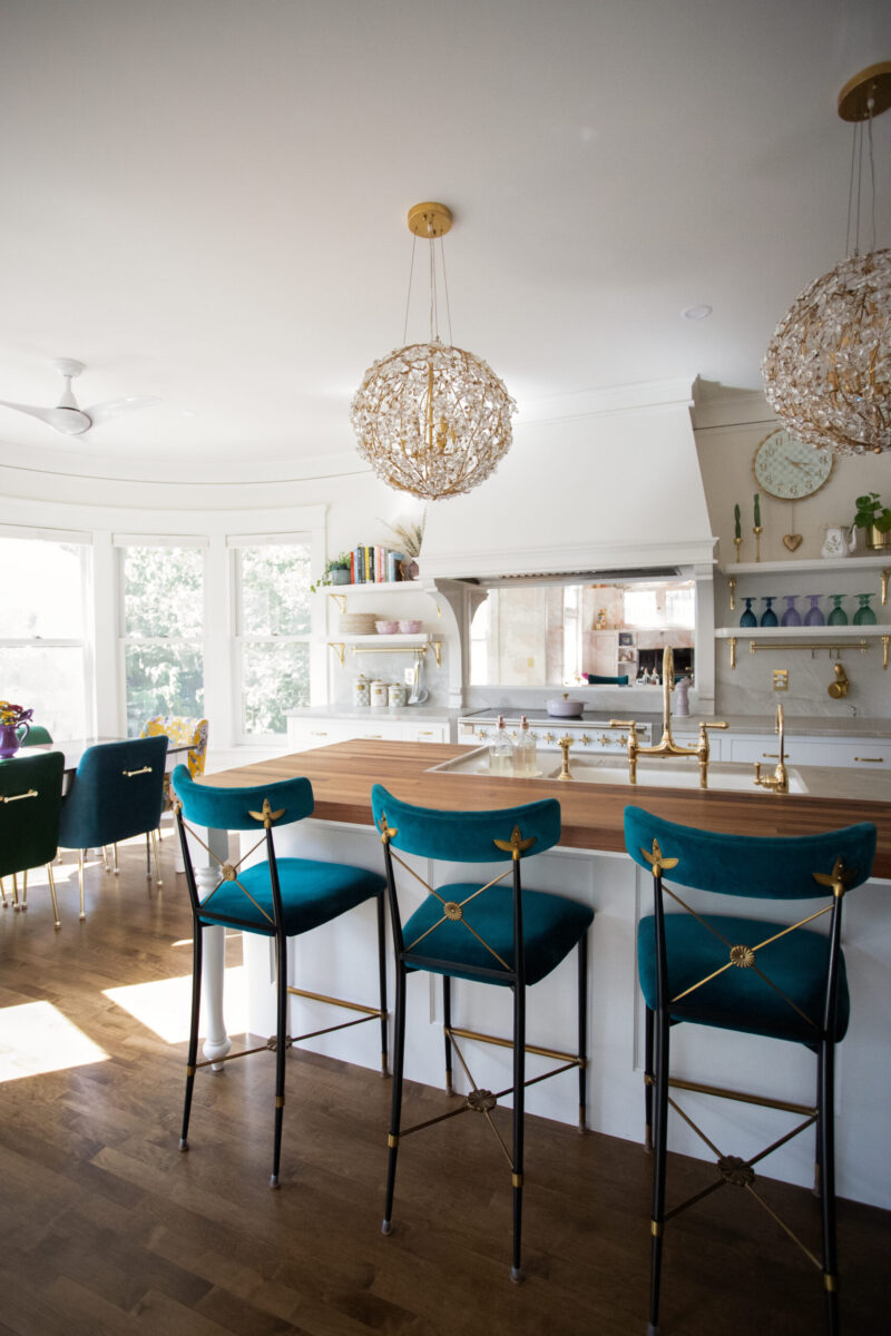 Twin Cities kitchen remodel's butcher block island, teal velvet barstools, crystal chandeliers.