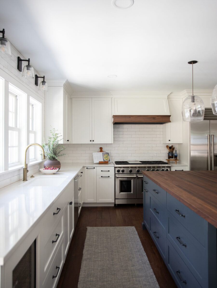 Bright Twin Cities kitchen renovation: white shaker cabinets, subway tile, dark wood floors, blue island, wood counter, brass faucet.