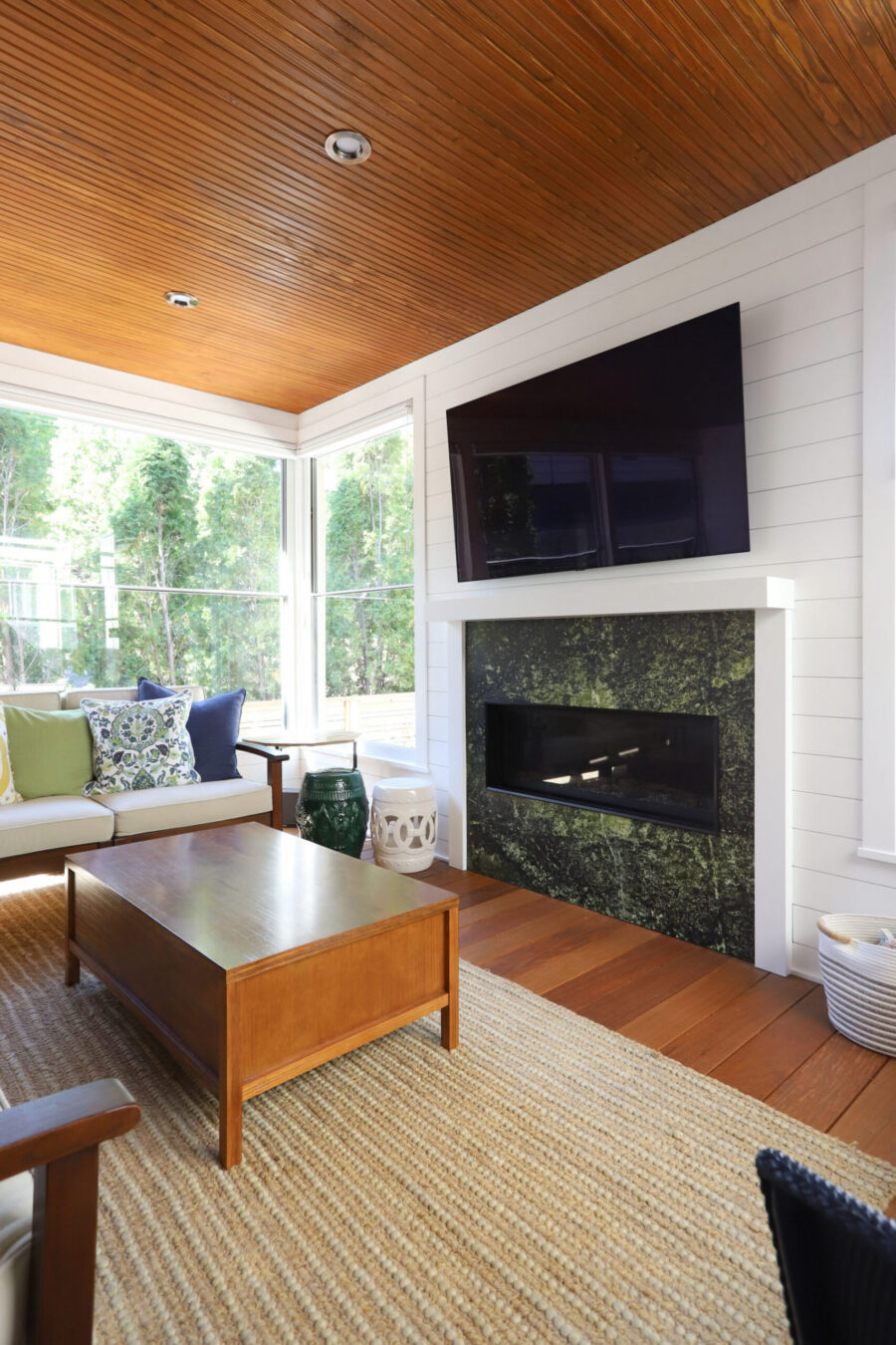 Sunroom renovation includes wood ceiling, shiplap, green marble fireplace, hardwood.