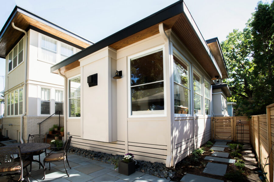 Contemporary exterior renovation adds large windows, light stucco, dark roof, paver patio.