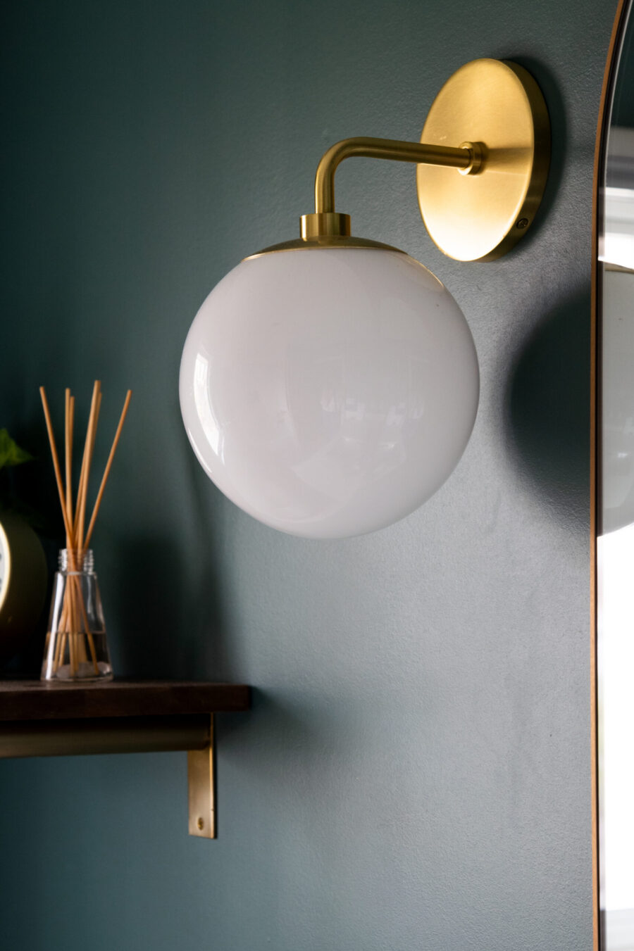 Brilliantly polished brass spherical sconce illuminates deeply emerald renovation-wall.