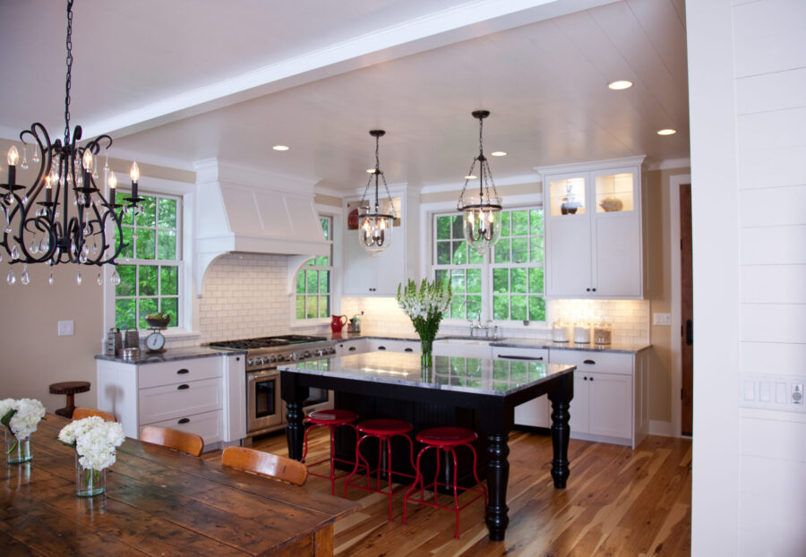 Twin Cities kitchen renovation has white cabinetry, a black island with red stools, and light hardwood floors.