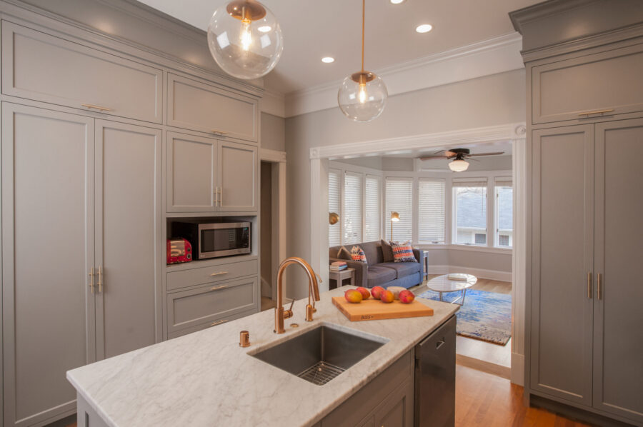 Twin Cities home renovation displays gray shaker cabinetry, marble island, copper faucet, bright lighting.