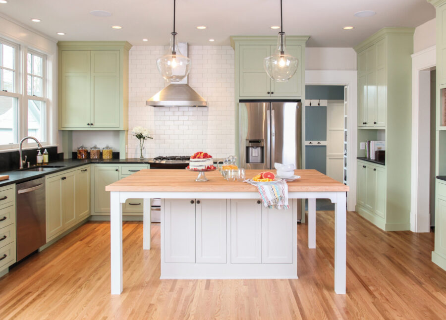 This bright kitchen remodel features light green cabinets, black counters, white subway tile, and a large wood-top island. Twin Cities home renovation.