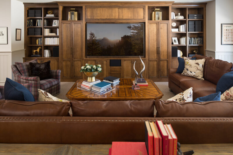 Custom wood built-ins frame a TV in this elegant living room. Brown leather sofas and a plaid armchair furnish the renovated Twin Cities interior.