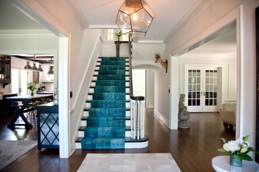 Renovated entryway boasts vibrant teal staircase, dark wood flooring, illuminated interior.