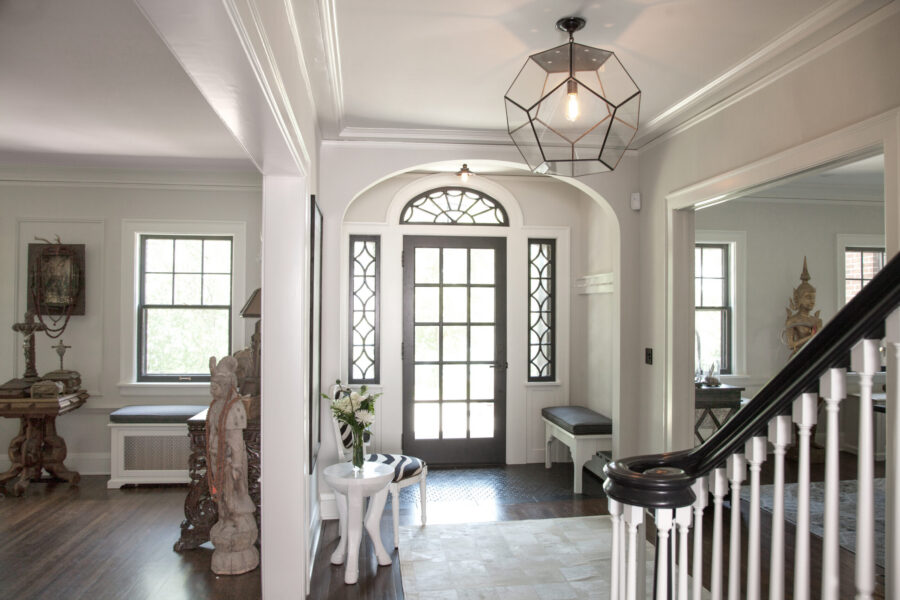 Luxurious entrance renovation features rich dark woodwork, pale walls, stunning geometric chandelier.