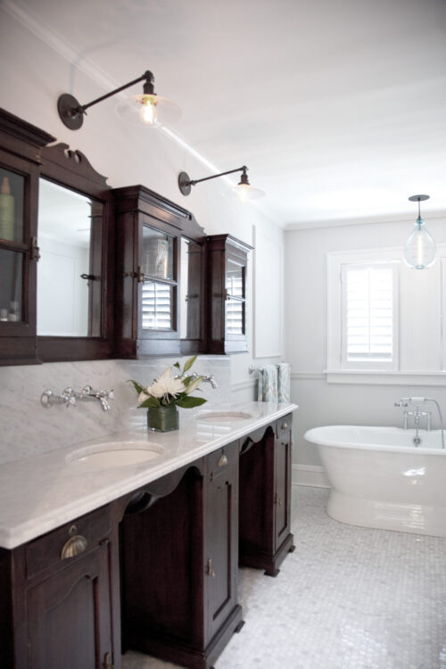Dark-wood vanities and marble-countertop feature glass-sconce lighting, freestanding tub.