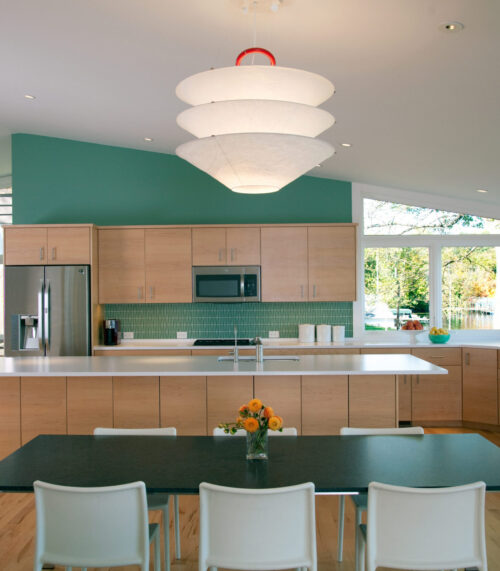 Open-plan kitchen features maple-cabinetry, green-tile-backsplash, white-quartz-counters, pendant-lighting, lakeview-windows