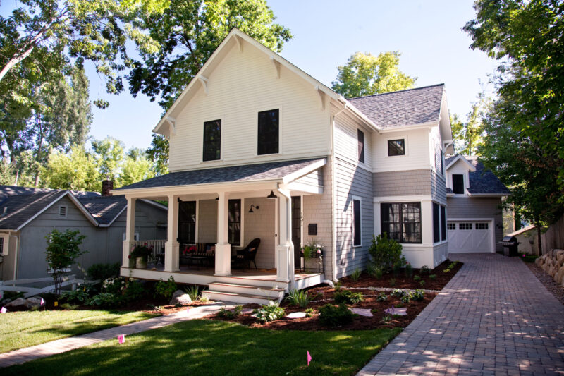 Modern farmhouse home renovation features white, gray siding, front porch, paver driveway.