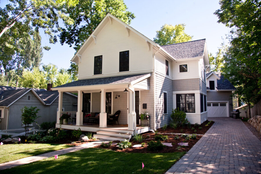 Modern farmhouse home renovation features white, gray siding, front porch, paver driveway.