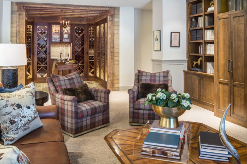 Basement remodeling creates custom wooden wine storage, inviting plaid upholstered armchairs.