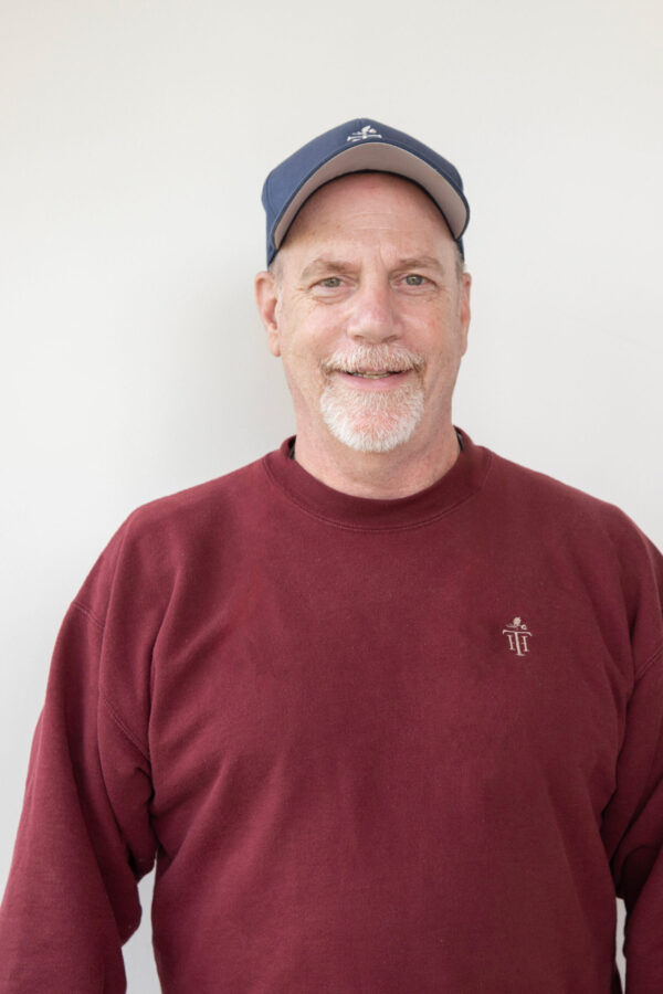Smiling man wears deep maroon long-sleeved sweatshirt, navy blue cap.