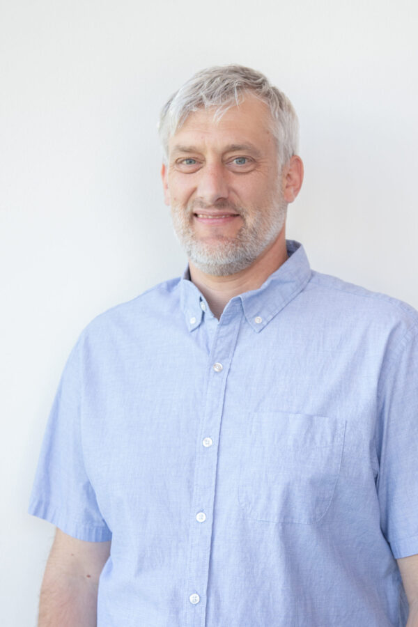 Smiling, gray-bearded, silver-haired gentleman dons a light-blue, short-sleeved, button-up.