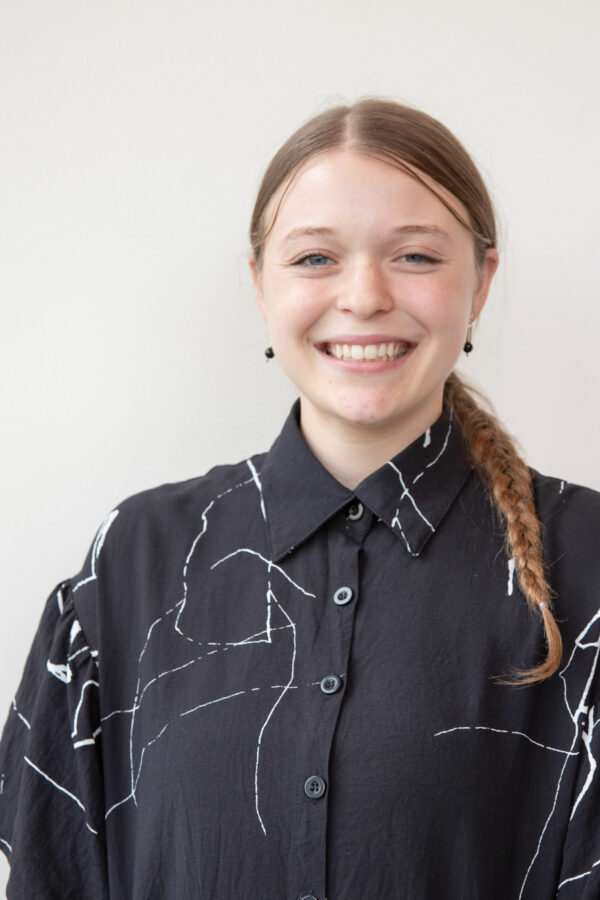 Professional portrait captures smiling individual, black patterned shirt, light background.