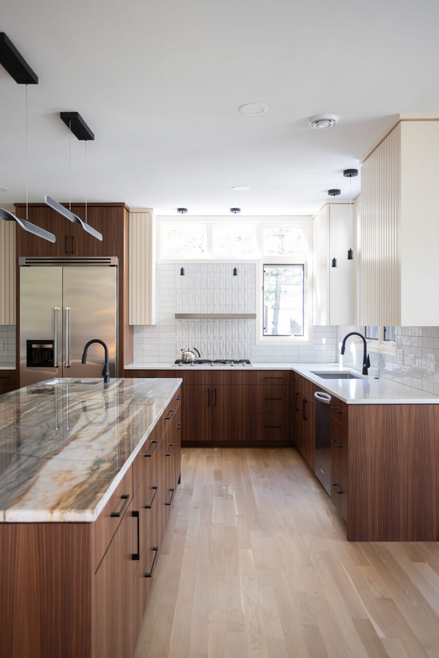 Twin Cities kitchen renovation: dark wood cabinetry, veined marble island, light floors, sleek lighting.