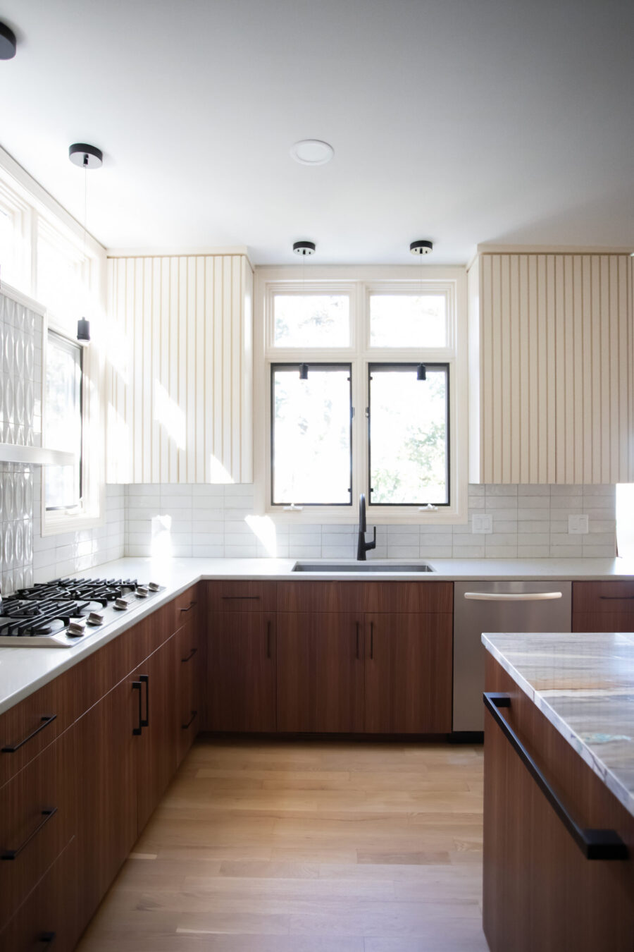 Contemporary kitchen remodel emphasizes dark cabinetry, light counters, ceramic tile backsplash.