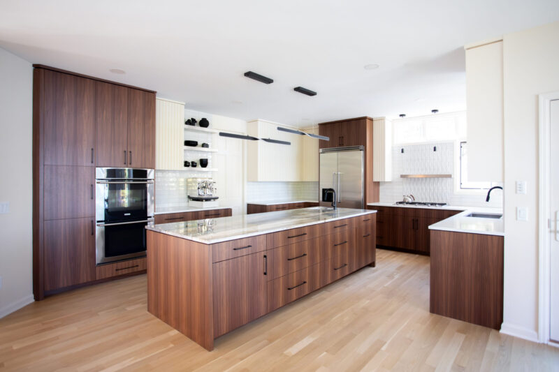 Kitchen renovation integrates rich wood cabinetry, light floors, and quartz counters.