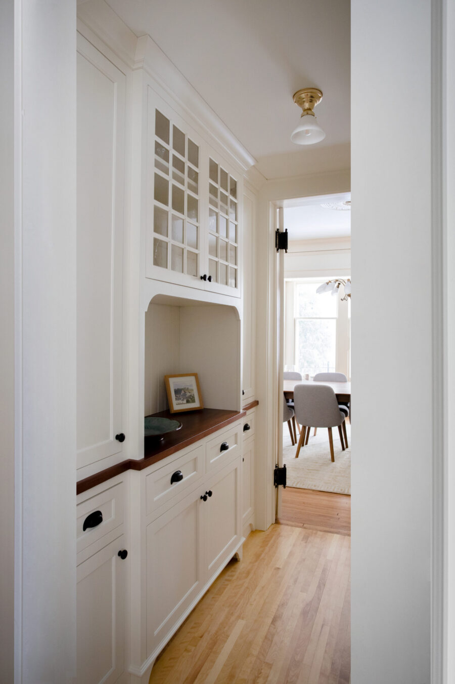 Twin Cities home renovation features custom white built-ins with glass, dark wood counter, light wood floors, and warm lighting.