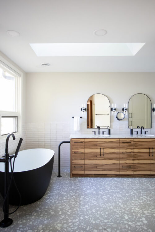 Bathroom has matte-black freestanding tub, walnut-grain vanity, large-skylight, polished-terrazzo-flooring