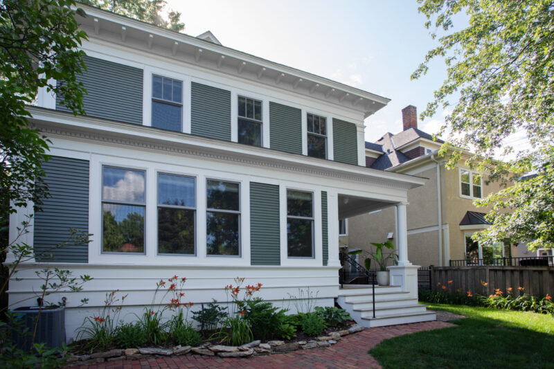 Classic-style home renovation features green siding, white trim, expansive porch.