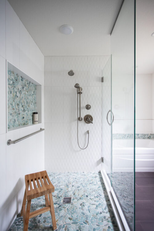 Twin Cities bathroom remodel: spacious walk-in shower, white textured tiles, blue pebble floor, glass enclosure.