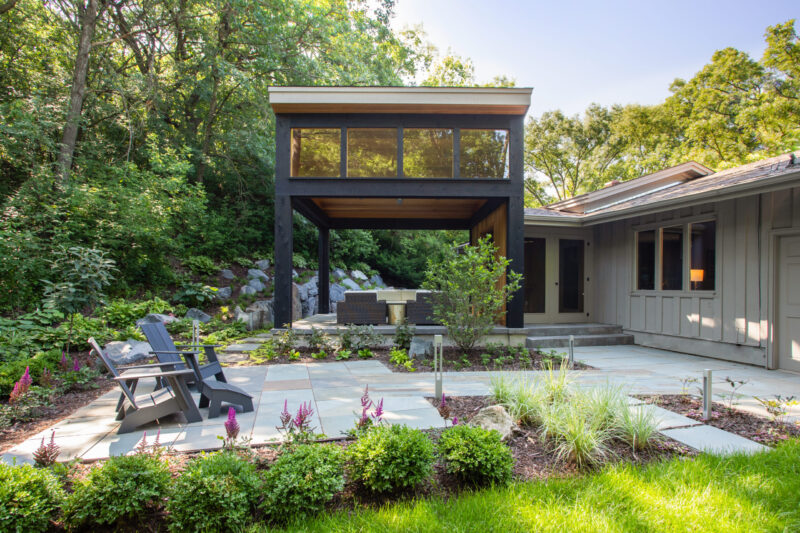 Modern black architectural addition, wood-ceilinged patio, flagstone hardscaping, gray home exterior renovation.