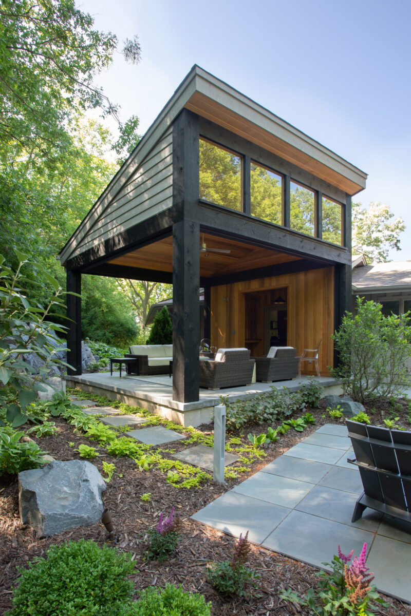 Modern design-build addition features shaded patio, timber ceiling, lush landscaping.