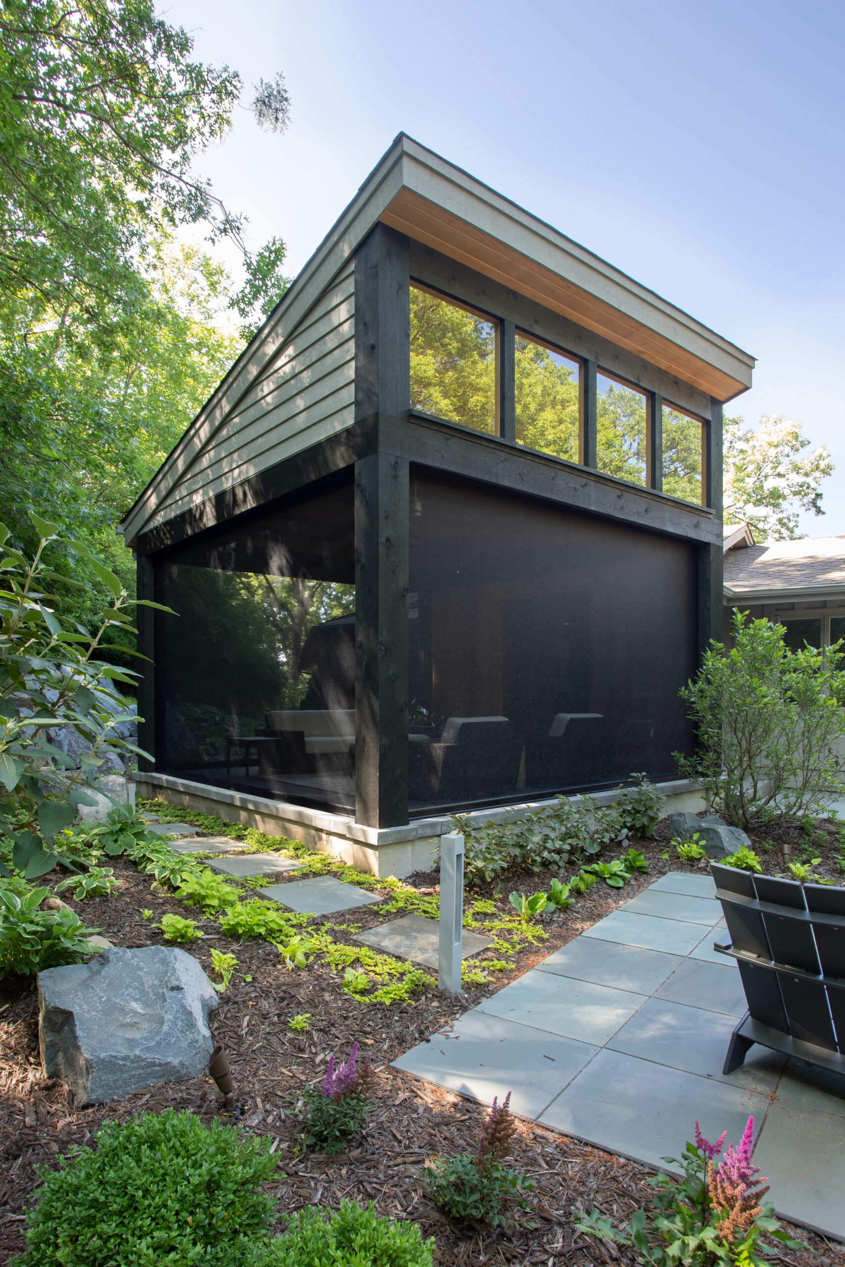 Charred-timber pavilion displays clerestory glazing, stone-paved pathways, lush plantings