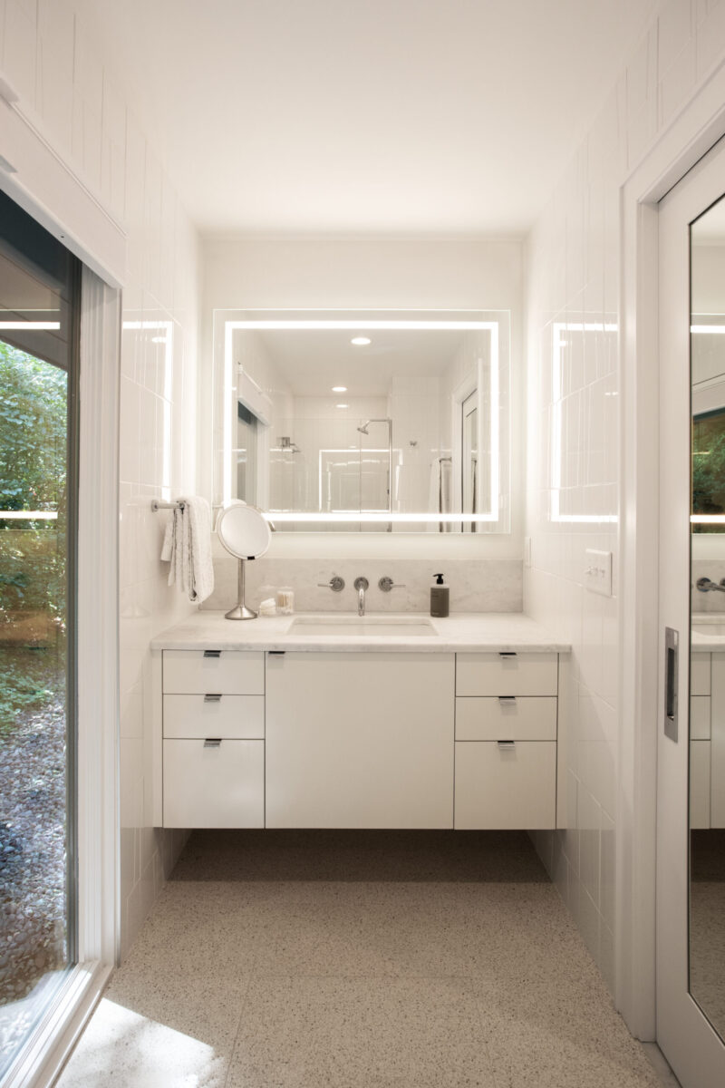 Modern bathroom renovation comprises floating vanity, backlit mirror, terrazzo floor.