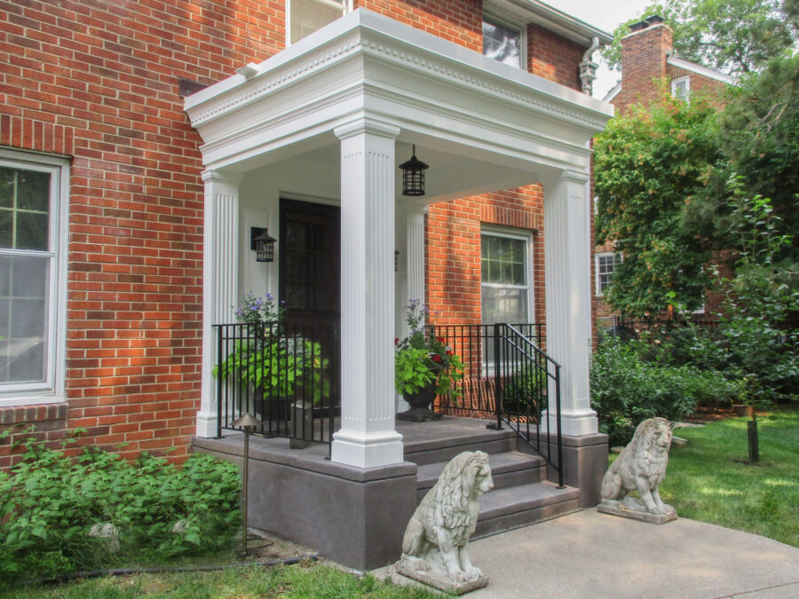 Stately white fluted-columned portico upgrades brick home entrance. Exterior design-build.