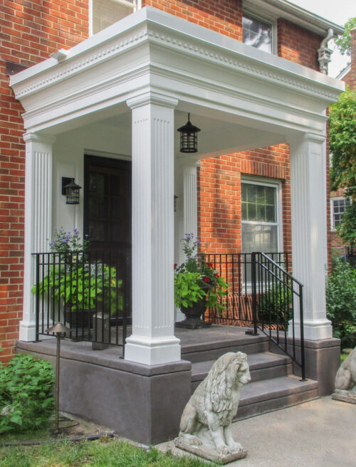 Stately white fluted-columned portico upgrades brick home entrance. Exterior design-build.