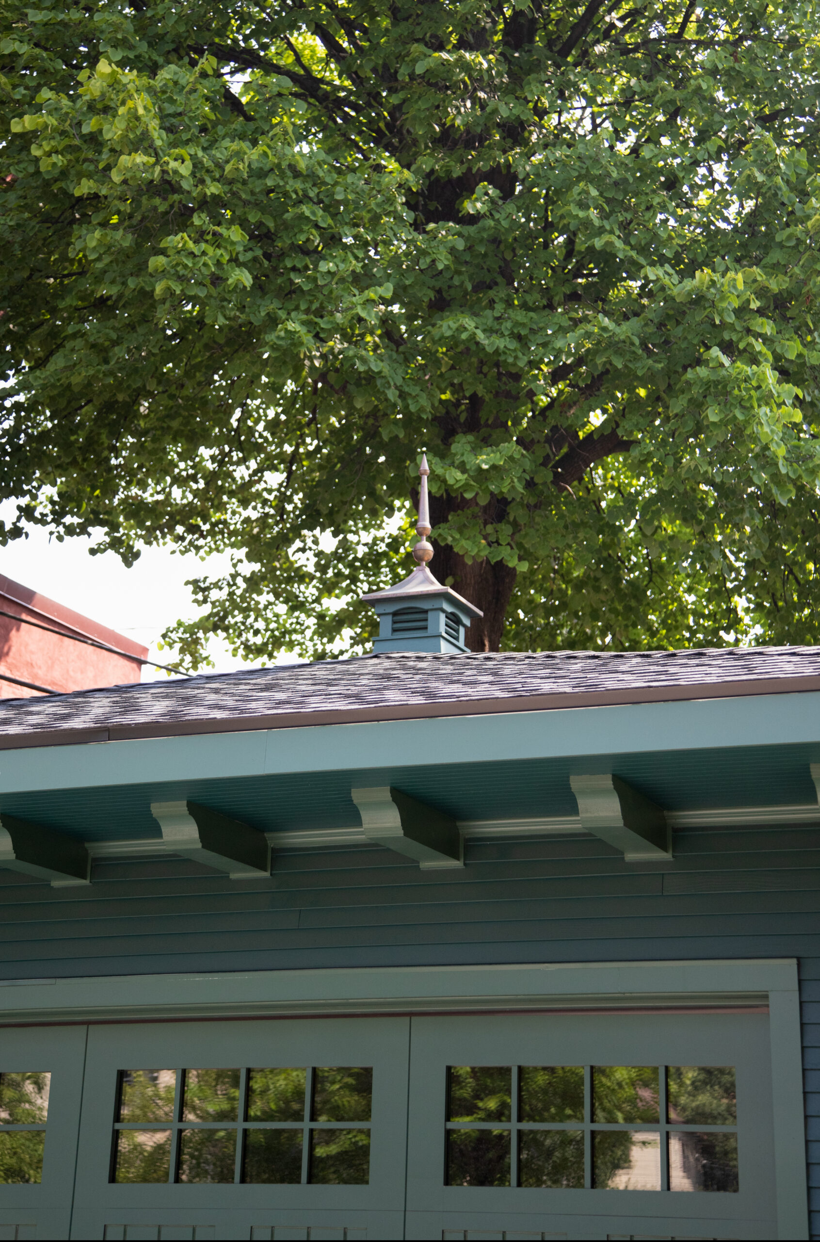 Turquoise-painted garage-facade features architectural cupola, turned finial, exposed rafters.