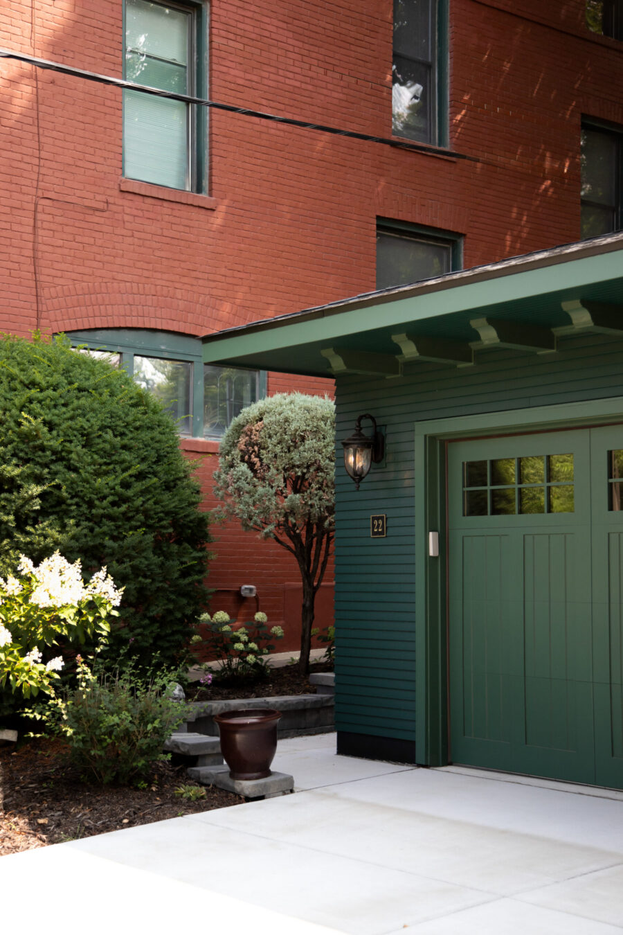 Green craftsman garage addition, new landscaping, complements red brick home.