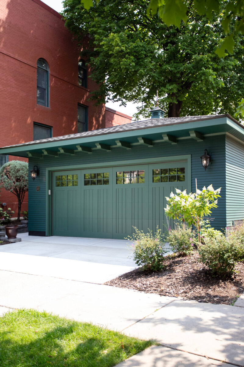 Renovated deep-green craftsman garage features paneled door with lighting.
