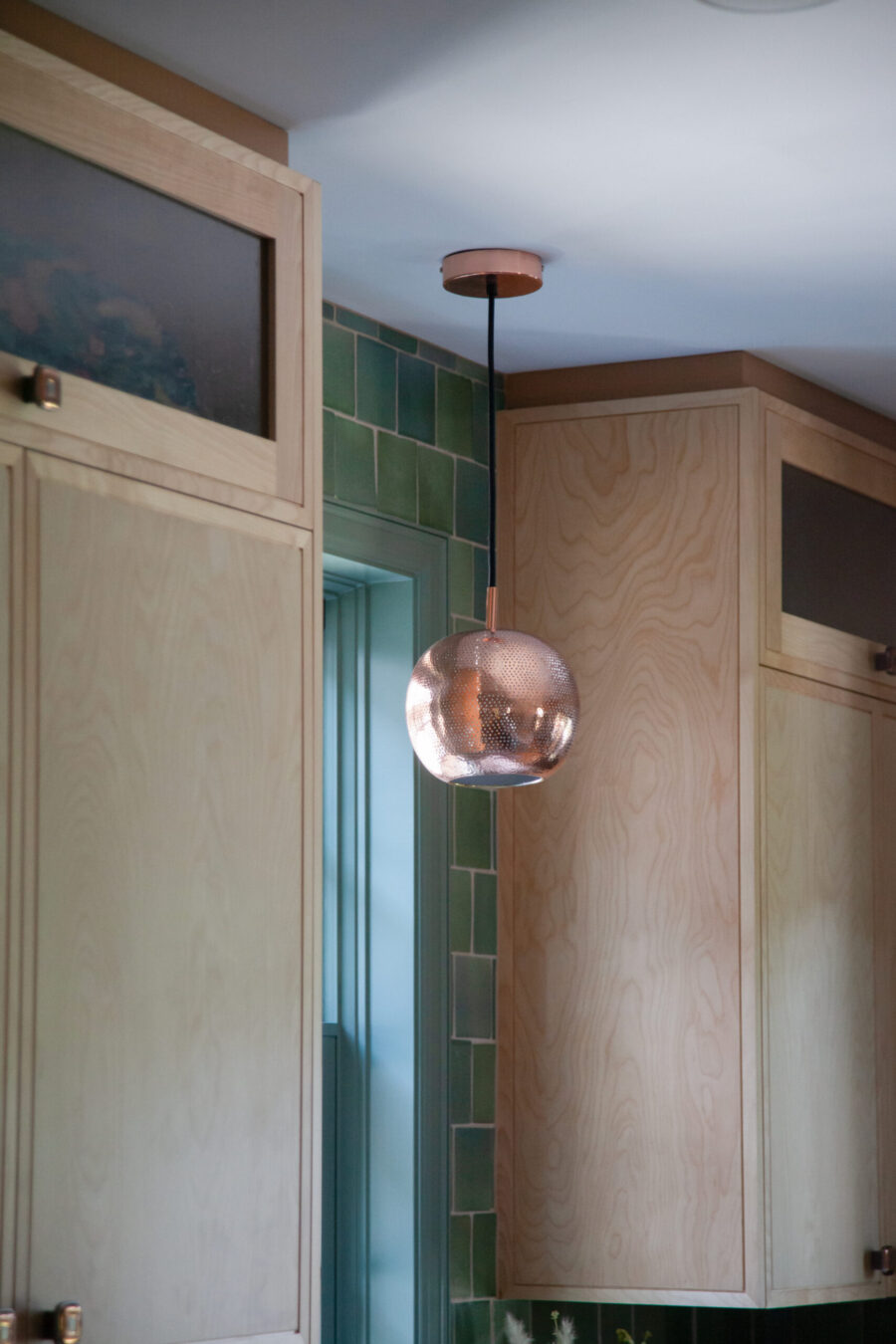 Twin Cities kitchen renovation boasts light wood cabinetry, green tile, copper pendant light.